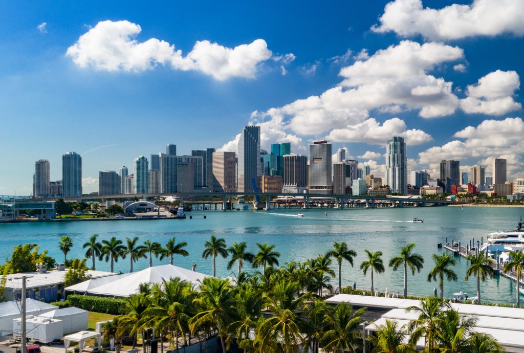 The downtown Miami skyline seen from a low elevation, with palm trees and Biscayne Bay in the foreground, representing South Florida's post-pandemic housing market changes.